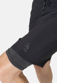 Schwarze Sportshorts aus glattem Material mit einem grauen Akzent am Saum. Verfügt über einen Kordelzugbund und einen dezenten Logo-Druck.