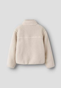 Veste en polaire crème, douce au toucher, avec un col, présentant une couture au dos et un design légèrement court. Pas de quincaillerie visible.