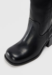Černá kožená kotníková bota s hladkým povrchem, čtveratou špičkou a středním blokovým podpatkem, vybavená jednoduchým šitím a elegantním, minimalistickým designem.