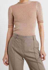 Bandeaul collar, kortekorte top in beige met verticale ribbels en contrasterende roestkleurige strepen; gekartelde zoomdetail op de mouwen.