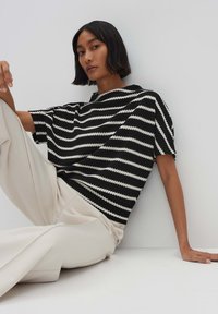 Zwart-wit gestreepte gebreide top met een relaxte fit, korte mouwen en een hoge halslijn, gecombineerd met crèmekleurige wijde broek.