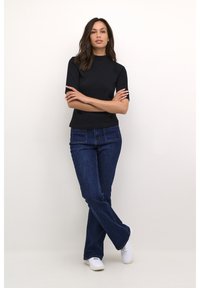 Black short-sleeve top with a high neck, paired with dark blue flared jeans and white sneakers. The ensemble features a fitted silhouette.