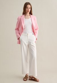Blazer rosa chiaro sopra una canotta bianca, abbinato a pantaloni bianchi a gamba larga e sandali marroni con cinturini. Tessuto morbido, vestibilità su misura.