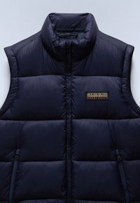 Mörkblå puffer-väst med hög krage, dragkedja fram och två dragkedjefickor på sidan. Har en kviltad textur och ett märkespatch på bröstet.
