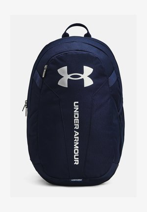 Mochila azul marino con un diseño estructurado, que presenta un destacado logo plateado, correas acolchadas y un bolsillo con cremallera en la parte frontal. Material impermeable.