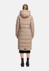 Abrigo largo acolchado beige con capucha, que cuenta con secciones acolchadas, un parche de logo negro en el dobladillo y una silueta estilizada.