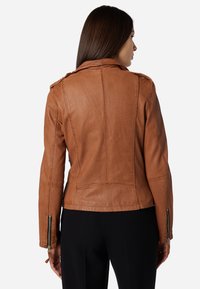 Braune Leder-Motorradjacke mit figurbetontem Design, sichtbaren Nähten und Reißverschlussakzenten an den Ärmeln. Matte Textur mit strukturierter Silhouette.