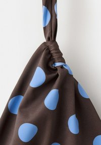 Brown fabric with large blue polka dots gathered and tied in a knot, hanging against a plain light background.