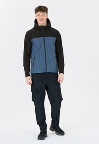 Kapuzenshirt mit einem Farbblockdesign in Blau und Schwarz, kombiniert mit schwarzen Cargo-Hosen und schwarzen Wanderstiefeln. Glattes Material, mit Reißverschlusstaschen.