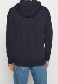 Felpa blu navy con cappuccio foderato, maniche lunghe, polsini e orlo a coste, e vestibilità rilassata. Il materiale appare morbido e strutturato.
