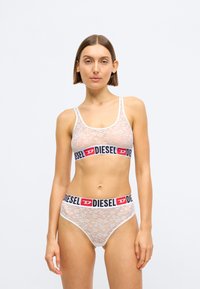 Hvit blonde bralette og matchende truser med en svart og rød "DIESEL" logo-bånd. Begge har en myk tekstur og tettsittende design.