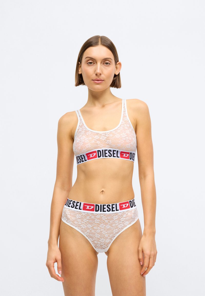 Bralette en dentelle blanche et culotte assortie avec une bande de logo "DIESEL" noire et rouge. Les deux pièces ont une texture douce et un design ajusté.
