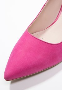 Escarpin en daim rose à bout pointu avec une texture lisse et une brillance subtile, présentant un design à découpe basse et un talon fin et élégant.