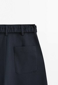 Pantalon noir avec une ceinture élastique, doté d'une poche arrière et d'un tissu lisse texturé avec un design simple.