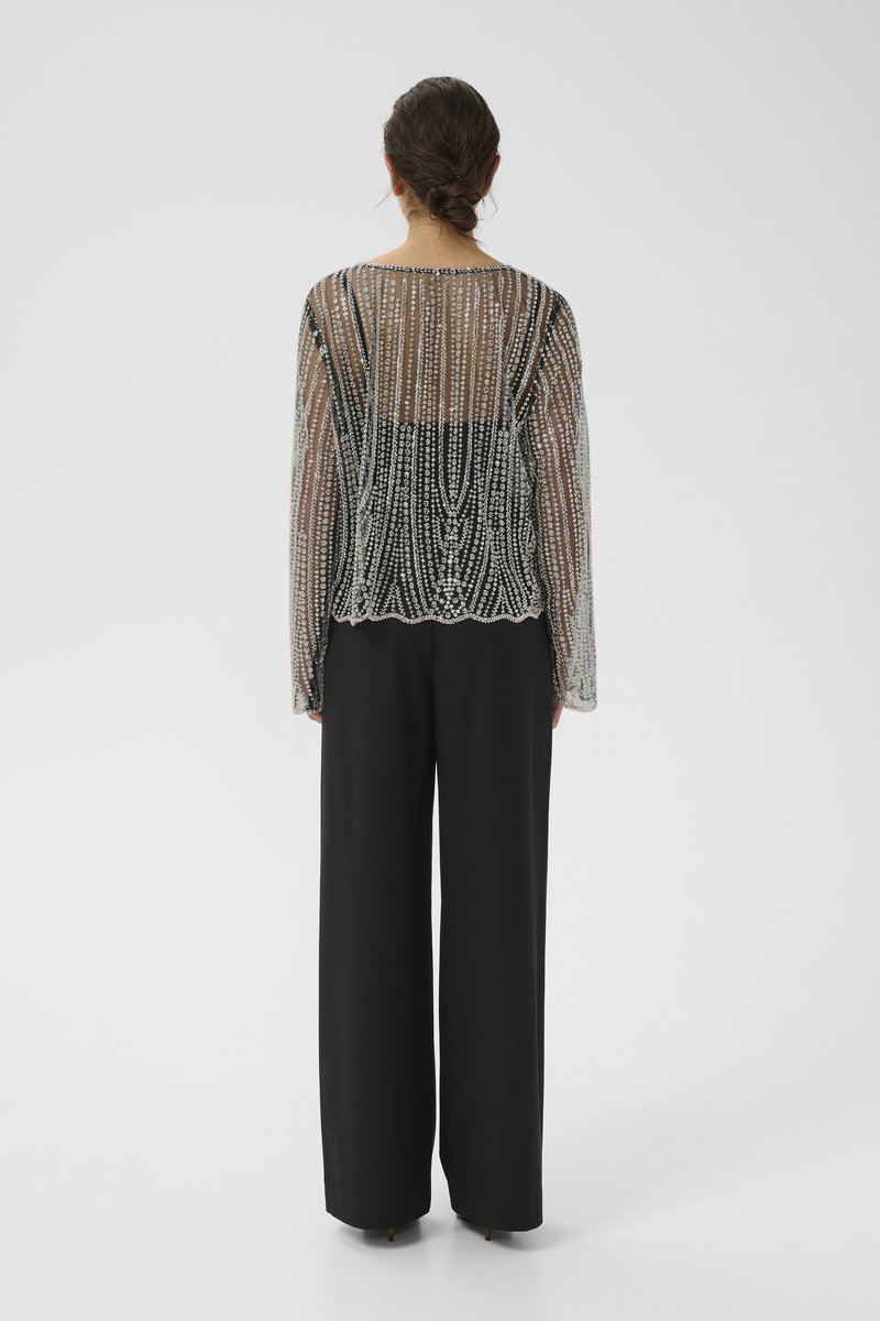 Transparent black beaded top with long sleeves, featuring a scalloped hem. Paired with high-waisted black wide-leg trousers.