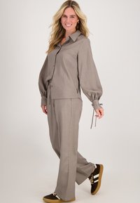 Beige gestreepte set met een blouse met knoopsluiting en ballonmouwen, voorzien van een trekkoorddetail, gecombineerd met een broek met brede pijpen en sneakers.