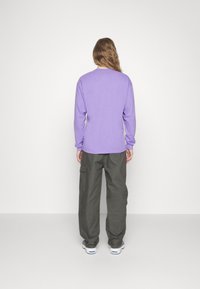 Långärmad lila skjorta med rund halsringning, tillsammans med löst sittande mörkgrå cargobyxor och vita sneakers.