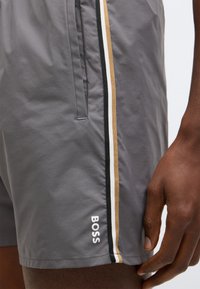 Sive hlače kratke od lagane tkanine s crno-bijelo-zlatnim prugama sa strane, s logotipom "BOSS" na rubu.