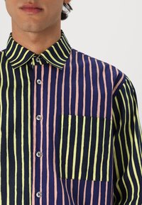Camisa a rayas con líneas verticales en azul marino, rosa y verde neón. Diseño con cuello, bolsillo en el pecho y cierre de botón.