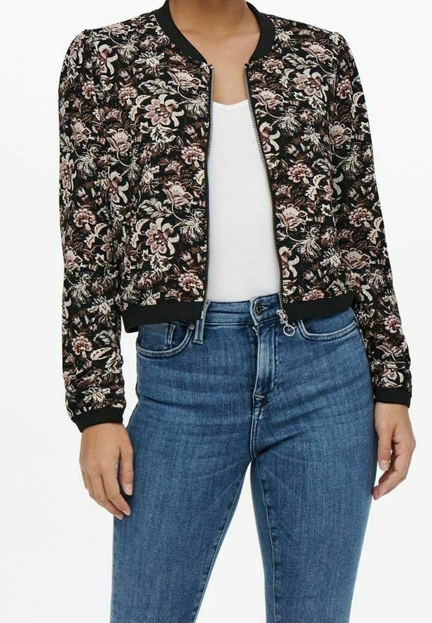 Veste bomber à motifs floraux sur fond noir, avec des poignets et un col côtelés, et une fermeture éclair. Associée à un jean bleu.