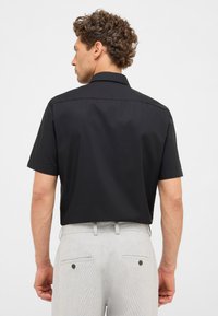 Korte mouwen zwarte shirt gemaakt van een gladde stof, met een klassieke kraag en een getailleerde pasvorm, gecombineerd met lichtgrijze broek.
