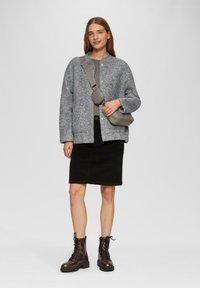 Grau strukturierte Jacke mit Rundhalsausschnitt, schwarzer Jeansrock und braunen Schnürstiefeln. Kleine graue Umhängetasche als Akzentdetail.