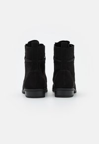 Bottines en daim noir avec un talon légèrement relevé, dotées d'un design minimaliste et d'un accent enveloppant autour de la tige.