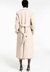 Beige wrap coat with a belt, tailored design, long sleeves, and a split back. Smooth texture, minimal detailing, and a clean silhouette.