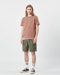 Brun bomulls t-shirt lager ovanpå en vit topp, kombinerad med gröna shorts, vit och svart randiga strumpor och bruna sneakers.