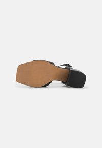 Schwarze High-Heel-Sandale mit quadratischer Zehenpartie und Knöchelriemen. Verfügt über ein elegantes, strukturiertes schwarzes Obermaterial und eine hellbraune Gummisohle.