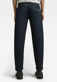 Donkerblauwe broek van gladde stof met een ontspannen pasvorm, voorzien van twee achterzakken en omslagzomen, gecombineerd met zwarte chunky schoenen.