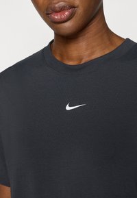 Tamsiai pilka medvilninė marškinėliai su klasikinio stiliaus apvalia iškirpte ir mažymu baltu „Nike“ logotipu ant krūtinės. Lygus audinys ir trumpomis rankovėmis.