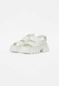 Sandali platform bianchi con larghe cinghie, dotati di un dettaglio con fibbia. Realizzati in materiale liscio, presentano una suola tozza e testurizzata.
