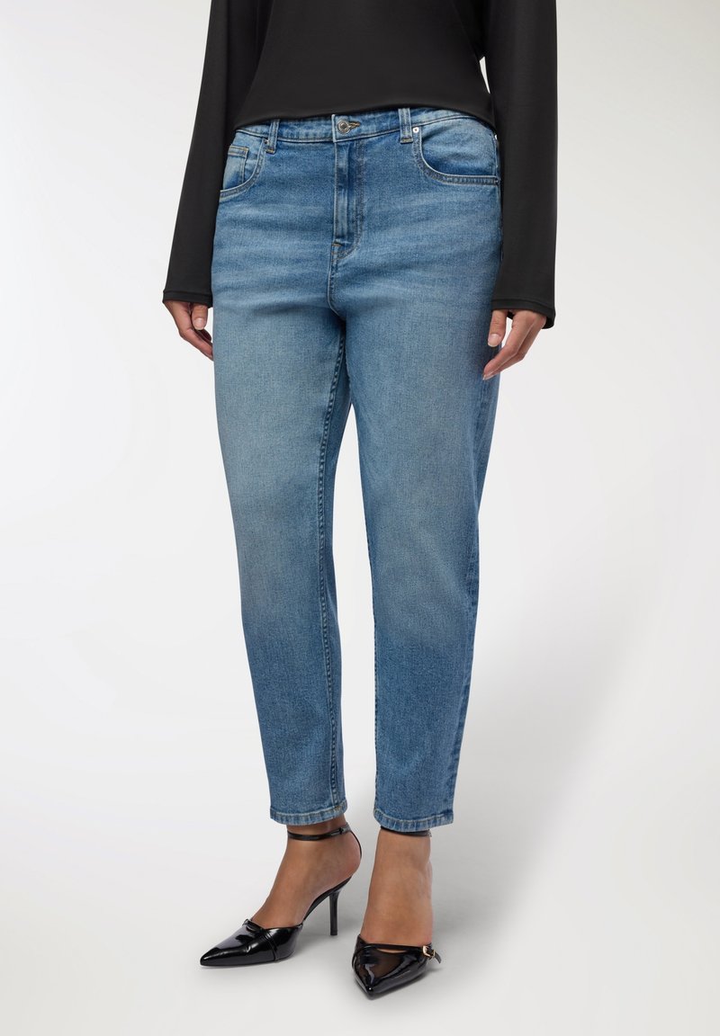 Jeans in denim azzurro chiaro con taglio dritto, design a cinque tasche e chiusura con bottone. Abbinati a scarpe con tacco alto nere.