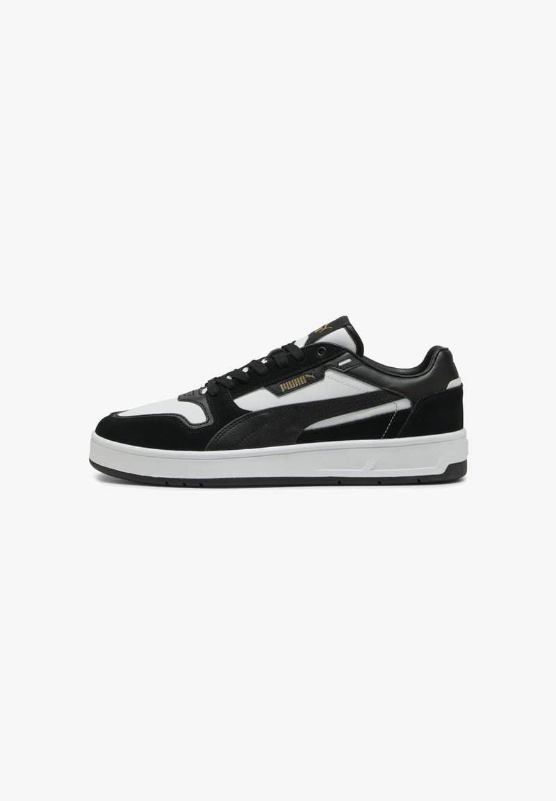 Baskets basses Puma noires et blanches avec laçage sur le devant, panneaux en daim et cuir, semelle blanche, et logo Puma sur le côté et la languette.