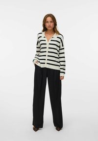 Gestreifter Cardigan in Creme und Schwarz mit Kragen und Knopfverschluss, kombiniert mit schwarzen weiten Hosen. Glatte Textur, lässige Passform.