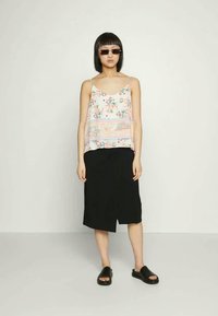 Top sem mangas com estampado floral em tons pastel, combinado com uma saia assimétrica preta e sandálias slides pretas. Tecido suave, ajuste relaxado.