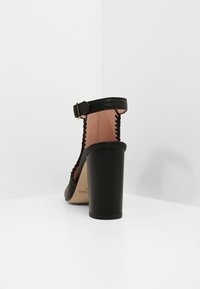 Černé sandály na vysokém podpatku s texturovaným povrchem, páskem kolem kotníku a opletenými detaily. Pevný blokový podpatek s světlou podšívkou.