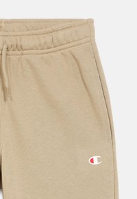 Μπεζ φόρμα με ελαστική μέση, ρυθμιζόμενο κορδόνι και μικρό λογότυπο στη χαμηλή πλευρά του ποδιού. Μαλακό ύφασμα με ομαλή υφή.