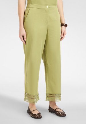 Lysegrønne bukser med lige ben og hæklet blonderkant, båret med mørkebrune vævede flade sko og en matchende armbånd.