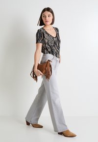 Blusa de manga corta a rayas negras y beiges, jeans de pierna ancha en gris claro, botas de tacón de ante marrón y un bolso de flecos marrón.