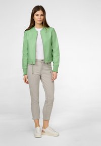 Mintgrüne Bomberjacke mit gerippten Bündchen, kombiniert mit hellgrauen Skinny Jeans und weißen Sneakers mit strukturiertem Akzent.
