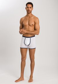 Valkoiset boxerit, joissa on tummansininen vyötärö ja saumat. Pehmeää kangasta, tiukasti istuva malli, jossa on etupussi tukea varten. Ei kuvioita.
