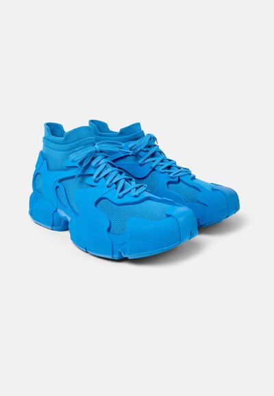 Modré sportovní boty s texturovaným síťovým svrškem a gumovými překryvy. Mají límec ve stylu ponožky a silnou podešev se vysoce tvarovaným designem.