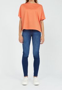 Oranžové tričko s krátkým rukávem a volným střihem, spárované s modrými skinny džíny a bílými teniskami se šněrováním a platformovou podrážkou.