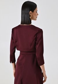 Burgunderfarbendes, kurzes Kleid mit Drei-Viertel-Ärmeln, glatter Satin-Textur und tailliertem Schnitt, das an der Taille eine dezente Naht aufweist.