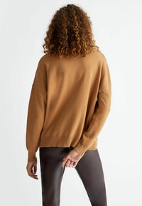 Pull marron tricoté à coupe décontractée, épaules tombantes et manches longues, associé à un pantalon marron foncé ajusté. Design simple, sans motifs.