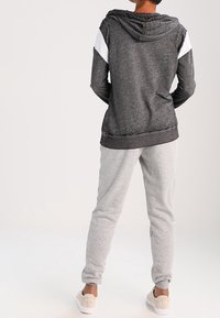 Šedá mikina s bílými akcenty na ramenech, vybavená kapucí na stažení a žebrovanými manžetami. Doplněna světle šedými tepláky z měkké tkaniny.