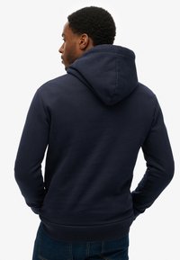 Sudadera azul marino con capucha, puños y dobladillo de canalé, hecha de una tela suave. Presenta una textura sutil sin patrones o acentos visibles.