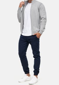 Grå lynlås-genser med høj krave, kombineret med marineblå joggingbukser og hvide sneakers. Genseren har ribstrikkede skulderdetaljer.